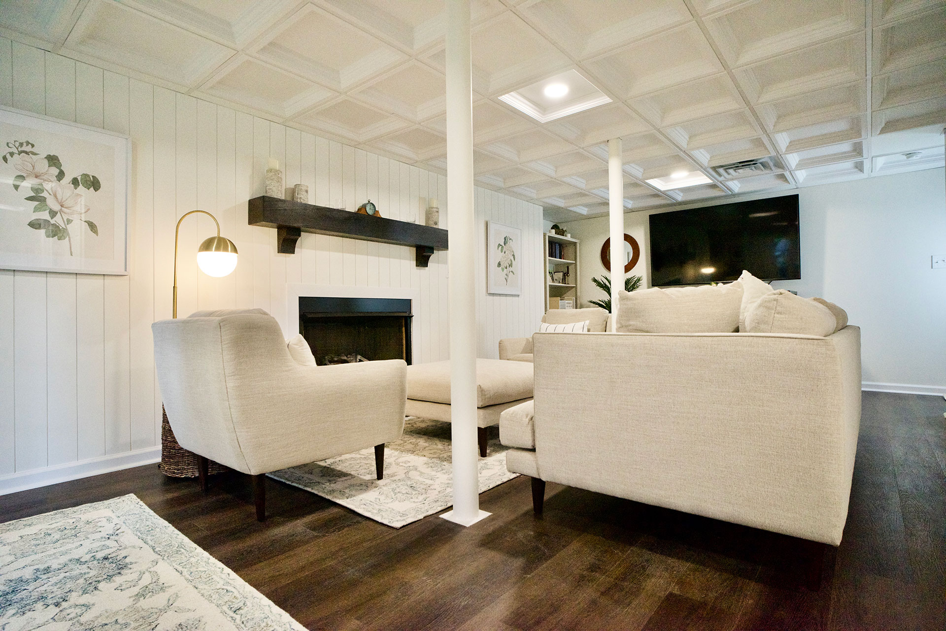 Basement finish with soft white walls, dark wood mantle over the fireplace